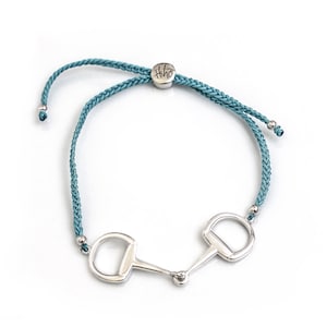 May include: Teal braided cord bracelet with a silver equestrian bit charm and a silver tag with the word "HiHo" on it.