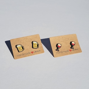 May include: Two pairs of wooden earrings on brown card stock. One pair features a beer mug design and the other pair features a wine glass design. The card stock has the text "Handmade with love" printed on it.