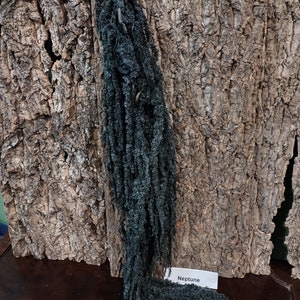 May include: A dark blue dried flower arrangement with a white tag that says "Neptune". The flower arrangement is hanging from a piece of cork bark.