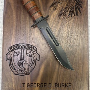 May include: A wooden plaque with a military-style knife and etched text. The plaque features the word "DARKHORSE" and a horse head design. Etched text includes "GARRY OWEN", "LT GEORGE D. BURKE", and "LIVIN THE GARRYOWEN DREAM".