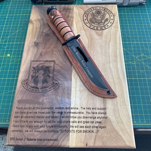 May include: A wooden plaque with a knife and sheath, featuring the text "170th Military Police Company" and the U.S. Army emblem. The plaque also includes a message and the text "DUTY, JUSTICE AND HONOR."