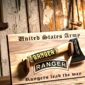 May include: Wooden plaque with a decorative axe, featuring the text "United States Army" and "Ranger". The axe has a wooden handle and a black blade. The plaque also includes the phrase "Rangers lead the way".