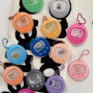 May include: A collection of 12 colorful round keychains with different cartoon animal characters inside. Each keychain has a silver chain and the text "SVT" on the bottom.