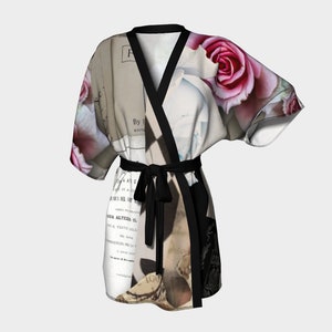 May include: A floral print kimono robe featuring pink roses and vintage book pages. The robe has a black trim and a matching tie belt. The design incorporates text and a collage aesthetic, creating a unique and artistic garment.
