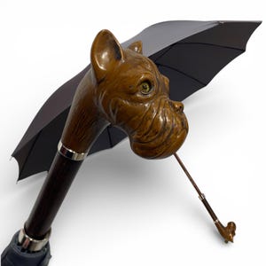 May include: A black umbrella featuring a handle carved as a dog's head. The dog's head is brown with detailed features and a silver ring. The umbrella is open, displaying the black canopy.