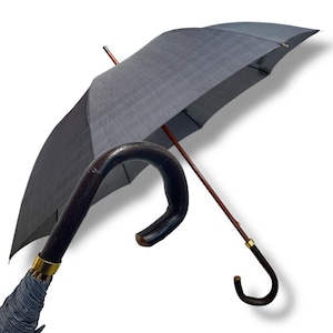 May include: A traditional grey umbrella with a wooden shaft and a dark brown, curved handle. The canopy has a subtle striped pattern. The handle is finished with a gold-coloured band. The umbrella is open, displaying its full size.