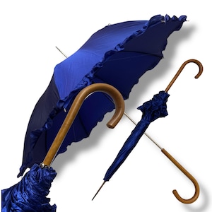 May include: Two blue umbrellas with wooden handles. One is open, revealing a ruffled edge, the other closed. The open umbrella has a dark blue canopy and a lighter blue ruffled trim. The handles are curved and made of wood.