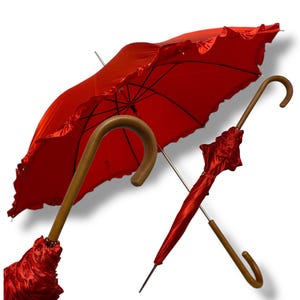 May include: Two red umbrellas with wooden handles. One is open, displaying a ruffled edge, the other closed. The open umbrella's canopy is a vibrant red, and the handles have a curved design.