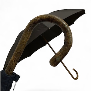 May include: A black umbrella with a curved, textured brown handle. The handle has a hook shape. The umbrella is partially open, revealing the black canopy. The umbrella is in a black fabric case.