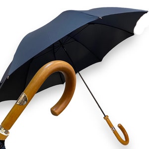May include: A navy blue umbrella with a wooden handle. The handle is curved and has a gold accent.