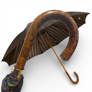 May include: A brown umbrella with a curved wooden handle and a striped canopy. The canopy features brown, yellow, and blue stripes. The handle has a gold-coloured metal band near the base.