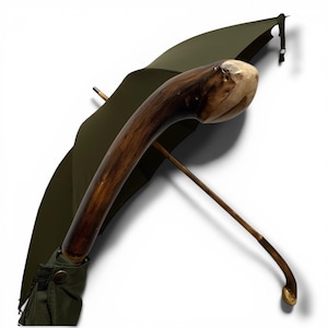 May include: An olive green umbrella with a distinctive wooden handle. The handle is dark brown with a light brown top. The umbrella's shaft is light brown. The umbrella is open, revealing its olive green canopy.