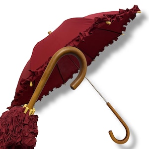 May include: A claret-coloured umbrella with a wooden handle and a frilled edge. The umbrella's canopy is a deep red hue, and the handle has a curved design. The umbrella is open, displaying its full shape and design.