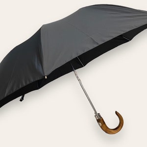 May include: A black and grey umbrella with a wooden handle. The handle is curved and has a silver metal tip.
