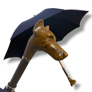 May include: A navy blue umbrella featuring a fox head-shaped handle made of wood. The handle is brown with a silver band. The umbrella is open, revealing its dark blue canopy. A smaller, matching umbrella is visible.