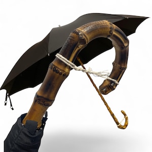 May include: A black umbrella featuring a curved bamboo handle. The handle is dark brown with carved details and a light rope tie. The umbrella's canopy is black, and the design is classic and elegant, suitable for various occasions.