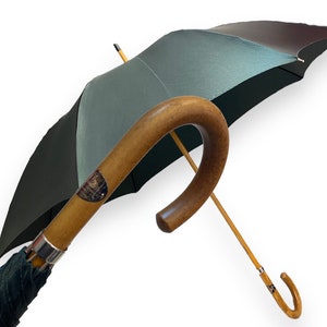 May include: A green and brown umbrella with a wooden handle. The handle is curved and has a silver band.