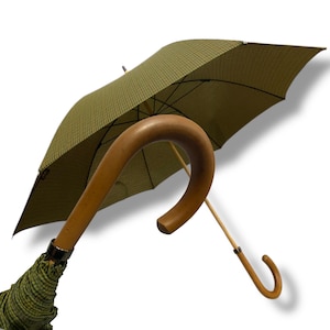 May include: Olive green and black check umbrella with a curved wooden handle. The umbrella's canopy is open, displaying a detailed pattern. The handle is light brown, and the umbrella's frame is visible.