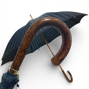 May include: An elegant umbrella with a curved wooden handle and a canopy with dark green and black stripes. The handle has a rich, brown finish, and the metal accents are gold-toned. The umbrella is partially open, displaying its design.