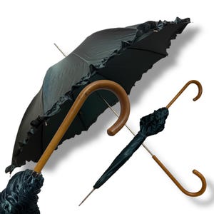 May include: Two black umbrellas with wooden handles are shown against a white backdrop. One is open, revealing a ruffled edge, the other closed. The handles have a curved, hook-like design. The umbrellas are for protection from the rain.