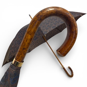 May include: A brown paisley-patterned umbrella with a curved wooden handle. The handle has a glossy finish and a gold-coloured metal band. The umbrella's canopy is a dark brown colour with a paisley design.