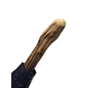 Puede incluir: Un mango de paraguas de madera con un acabado de madera de grano oscuro. El mango es liso y tiene una parte superior redondeada.