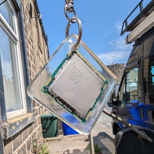 May include: A clear plastic keychain featuring a silver Intel Core i3-548 CPU chip. The chip is labelled with the text "Intel Core i3-548", "Intel Core i3", "SlotD Malay", "3.8AGHz/4M/PA", and "L1118549".