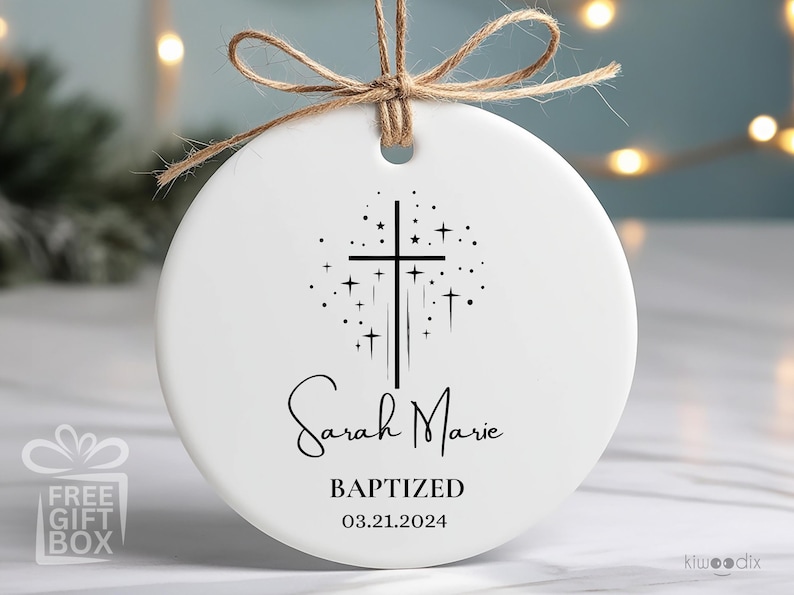 May include: White ceramic ornament with a black cross and stars design. The text "Sarah Marie Baptized 03.21.2024" is printed on the ornament.