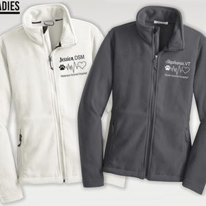 May include: Two fleece jackets, one white and one gray, with embroidered logos. The white jacket has the text "Jessica DSM" and a heart with a paw print and a heartbeat line. The gray jacket has the text "Stephanie VT" and a heart with a paw print and a heartbeat line.