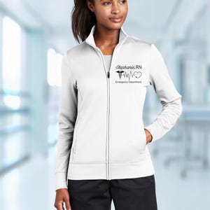 May include: White zip-up jacket with a black embroidered design featuring a medical symbol, a heart, and a heartbeat line. The text "Stephanie RN Emergency Department" is also embroidered on the jacket.