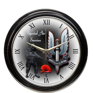 May include: Black-rimmed wall clock with a white face. The clock face features the words "Special Air Service", a soldier graphic, and the motto "Who Dares Wins". Roman numerals mark the hours.