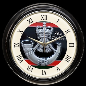 May include: A white clock face with Roman numerals and black hands. The clock face has a black and red background with a silver crown and a silver bugle. The text "The Rifles" is printed in black on the clock face.