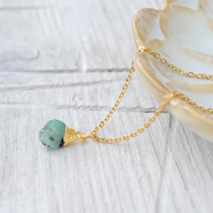 Könnte beinhalten: Eine goldene Kettenkette mit einem rohen Anhänger aus smaragdgrünem Stein.