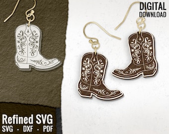 May include: A pair of gold-tone earrings featuring a brown cowboy boot design. The boots have a white floral pattern and are outlined in white.