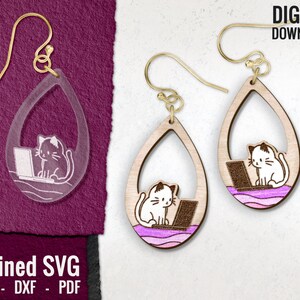 Puede incluir: Un par de pendientes de madera con forma de lágrima. Cada pendiente presenta un gato blanco sentado en un portátil con un fondo morado y rosa. Los pendientes están diseñados para descarga digital y vienen en formatos SVG, DXF y PDF.