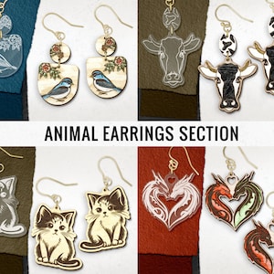 May include: Assortment of animal-themed earrings, including a pair of bluebird earrings, a pair of cow earrings, a pair of cat earrings, and a pair of dragon earrings.  The earrings are made of wood and have a variety of colors and designs.