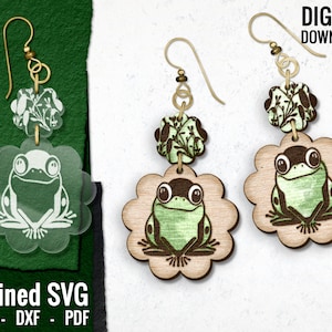 May include: A pair of wooden earrings with a green frog design. Each earring has a smaller floral charm above the frog. The earrings are on a white background.