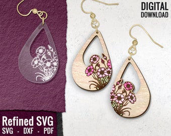 May include: A pair of wooden earrings with a teardrop shape and a floral design. The earrings are painted in shades of pink and green. The earrings are shown on a white background.