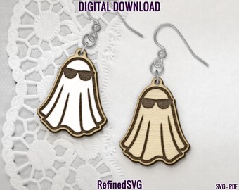 Op de afbeelding: Twee houten oorbellen in de vorm van een spook met zonnebril, hangend aan zilverkleurige haken. De geesten hebben een lichte houtnerf met een donkerbruine omtrek en zonnebril. De tekst "DIGITAL DOWNLOAD" en "RefinedSVG" zijn zichtbaar.