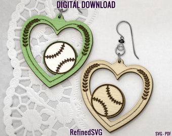 May include: A pair of wooden earrings shaped like hearts with a baseball inside each heart. The hearts are green and natural wood. The earrings are hanging from silver hooks.