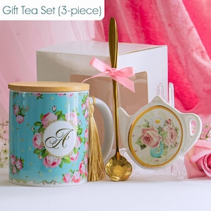 May include: A 3-piece gift tea set featuring a teal mug with floral design and the letter "A", a gold spoon, and a teapot-shaped saucer. The set includes a wooden lid and a gold tassel. The text "Gift Tea Set (3-piece)" is visible.