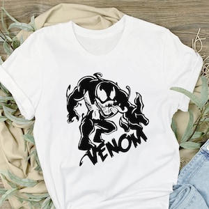 May include: White t-shirt with a black graphic of Venom, a Marvel Comics character, with the word "Venom" printed below the image.