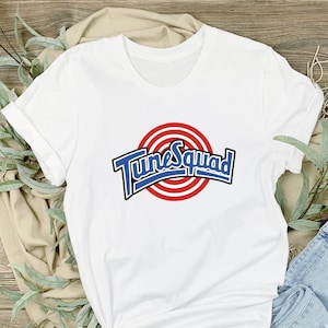 May include: White t-shirt with a blue and red "Tune Squad" logo featuring a basketball target graphic.