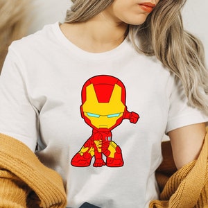 Puede incluir: Camiseta blanca con una imagen de dibujos animados de Iron Man en un traje rojo y amarillo, con una visera azul.