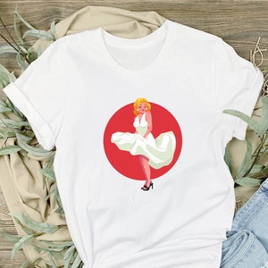 May include: White t-shirt with a red circle and a graphic of a woman in a white dress with her skirt blowing in the wind.
