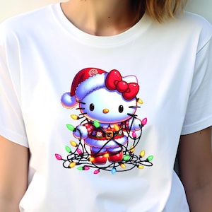 May include: White t-shirt featuring a festive Hello Kitty design. The cartoon character is dressed in a Santa hat and suit, adorned with a red bow and wrapped in colorful Christmas lights. A fun and cheerful holiday-themed graphic.