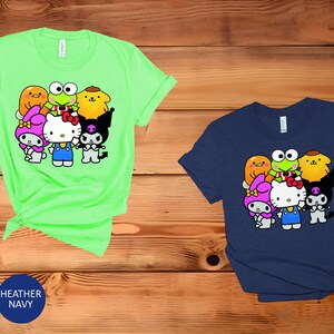 May include: A green t-shirt featuring a graphic of Hello Kitty and her friends, including My Melody, Keroppi, and Badtz-Maru. The graphic is in a cartoon style and shows the characters in various poses.
