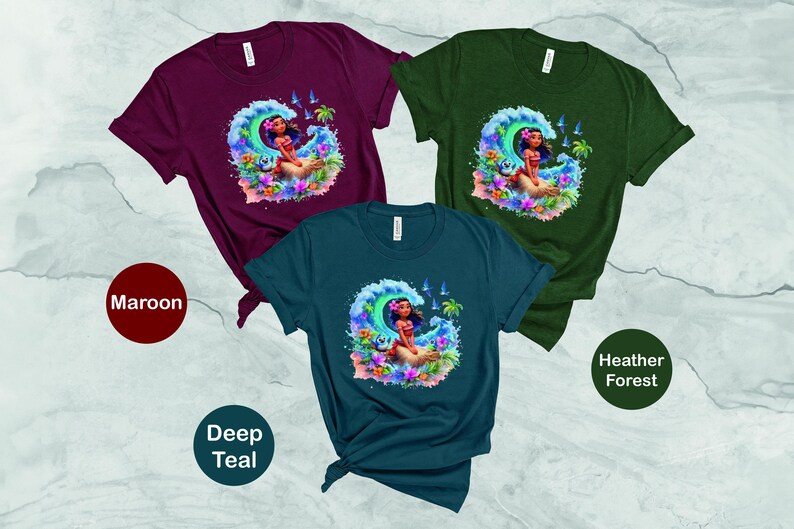 Peut inclure: Trois t-shirts avec une image de dessin anim&eacute; d'une femme sur une vague. Les t-shirts sont bordeaux, bleu sarcelle fonc&eacute; et for&ecirc;t chin&eacute;e.