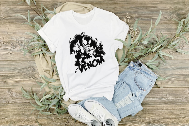 May include: White t-shirt with a black graphic of Venom, a Marvel Comics character, with the word "Venom" printed below the image.