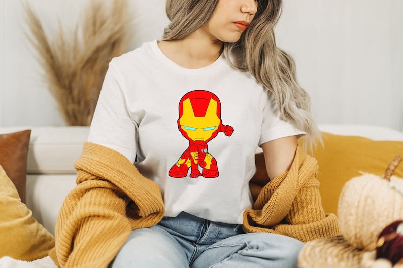 Puede incluir: Camiseta blanca con una imagen de dibujos animados de Iron Man en un traje rojo y amarillo, con una visera azul.